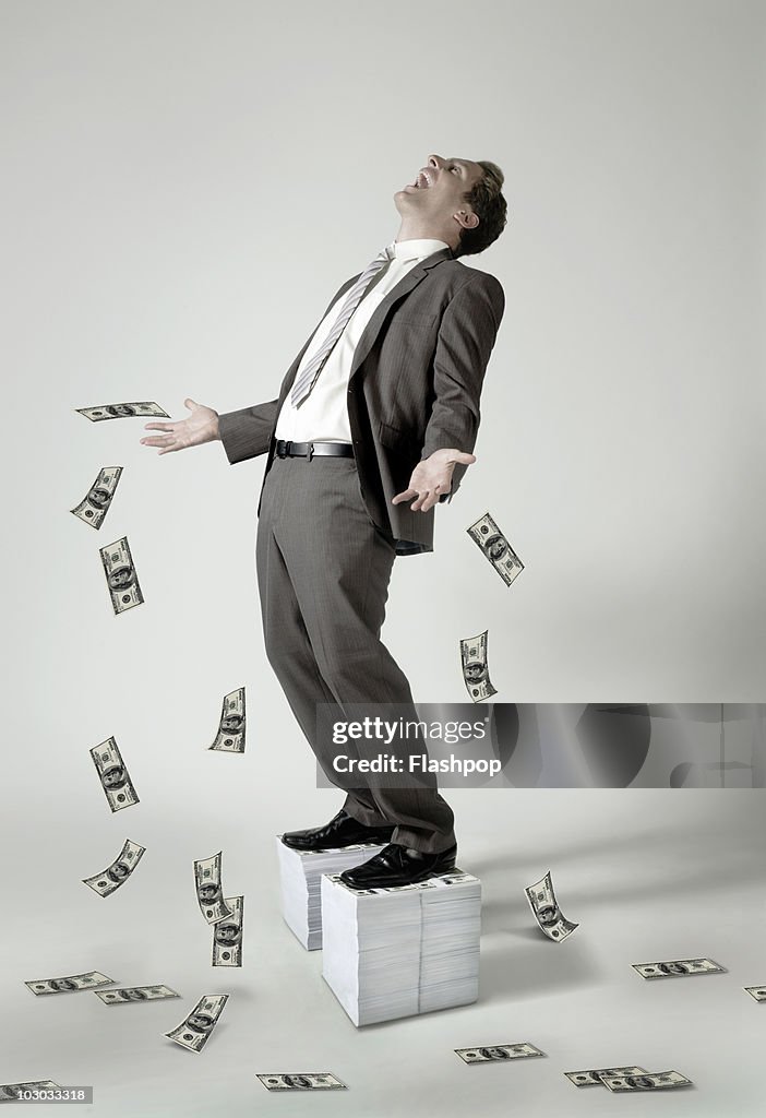 Businessman standing on large pile of dollar notes
