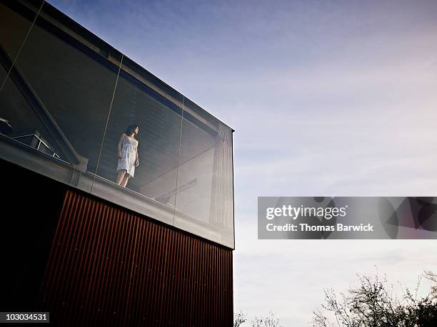 woman standing looking out window at sunset - einfamilienhaus modern stock-fotos und bilder