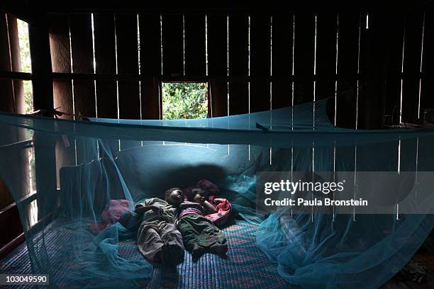 Yonta rests with her sister Montra and brother Leakhena, 4months under a mosquito bed net keeping dry from the monsoon rain July 18, 2010 in Prey...