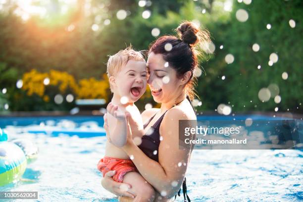 little boy with down syndrome having fun in the swimming pool with his family - physical disability stock pictures, royalty-free photos & images