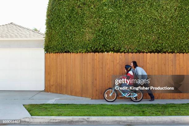 mixed race father teaching daughter to ride bicycle - family riding bikes with helmets stock pictures, royalty-free photos & images