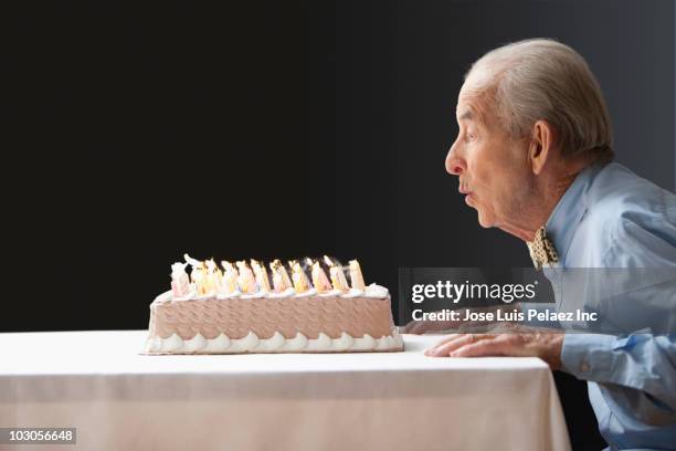 senior hispanic man blowing out birthday candles - longevità foto e immagini stock