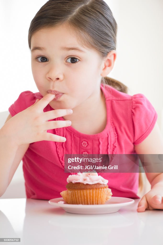 Mixed race girl licking frosting from finger