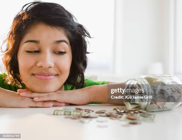 hispanic woman looking at change in glass jar - veleiding stockfoto's en -beelden