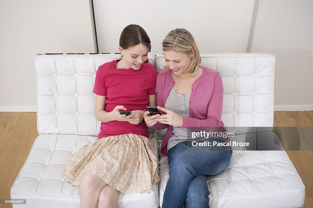 Woman with her daughter text messaging on mobile phones