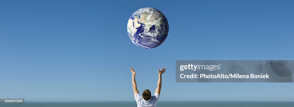 Arms raised reaching out to planet earth orbiting overhead