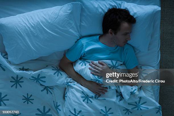 man lying awake in bed contemplatively looking away - above view of man sleeping on bed stock-fotos und bilder