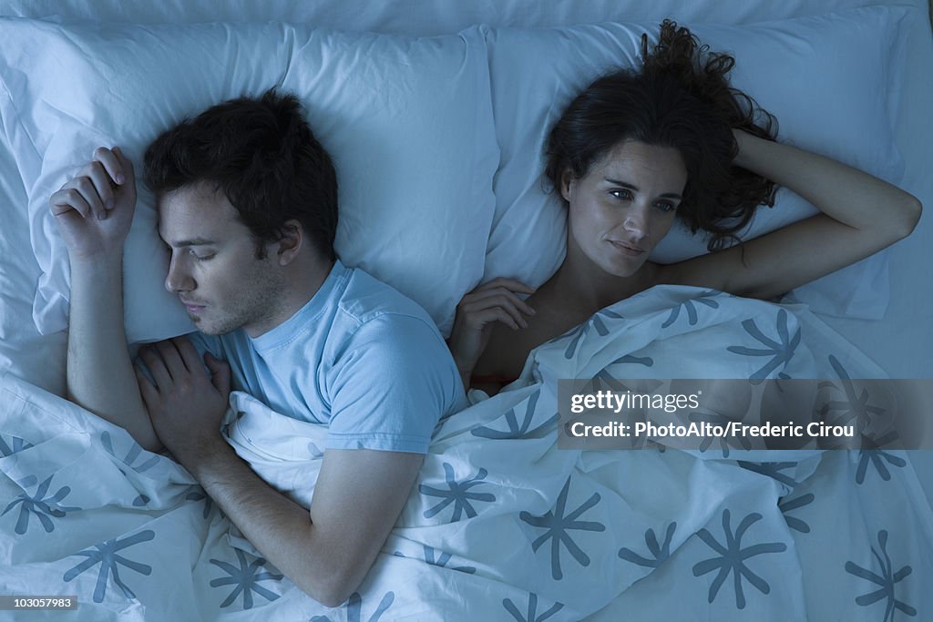 Couple lying together in bed, woman restlessly awake looking away