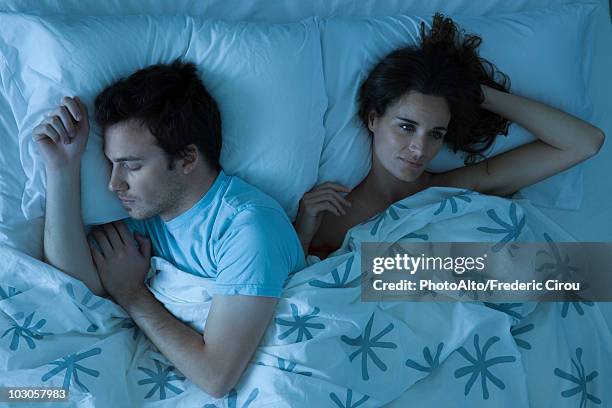 couple lying together in bed, woman restlessly awake looking away - above view of man sleeping on bed stock pictures, royalty-free photos & images