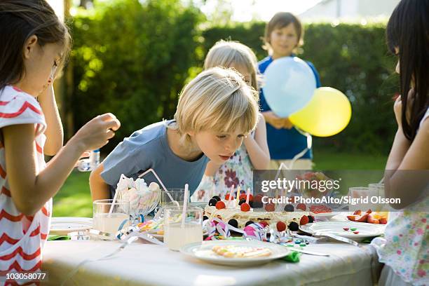 boy blowing candles on birthday cake at outdoor birthday party - barnkalas bildbanksfoton och bilder