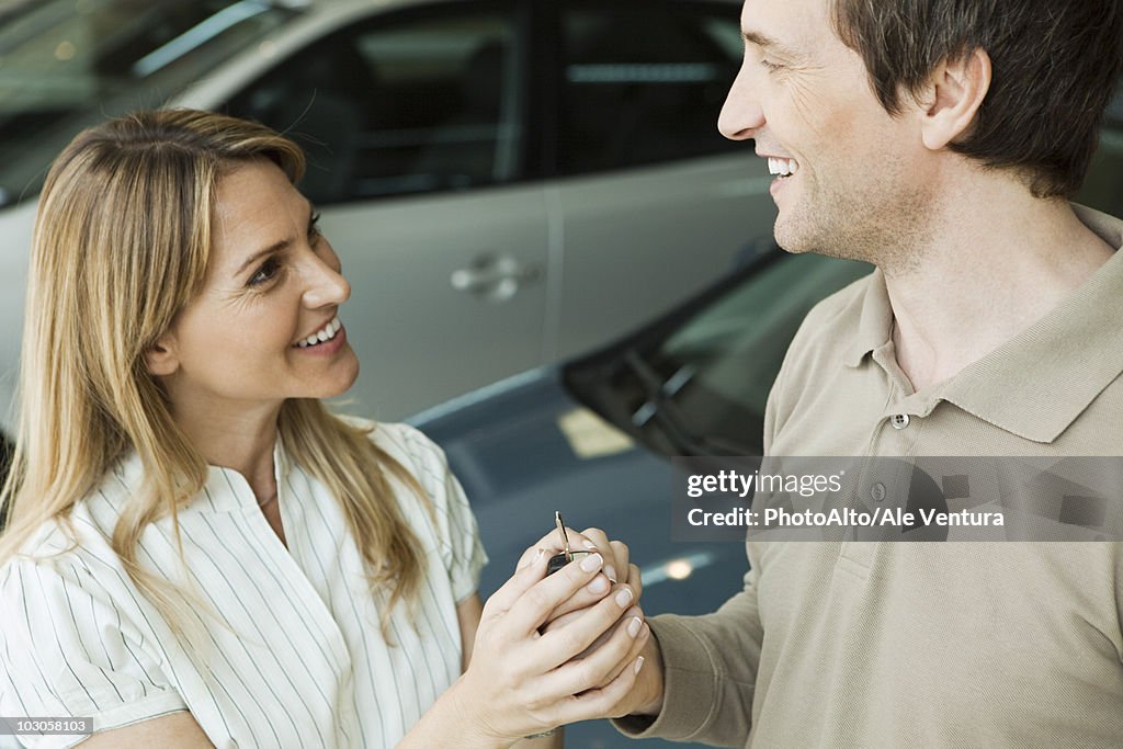 Couple in car dealership showroom with key to new car