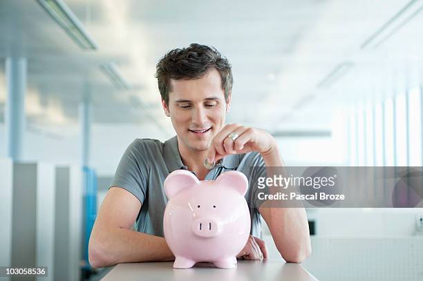 businessman inserting a coin into a piggy bank - saving up for a rainy day stock pictures, royalty-free photos & images
