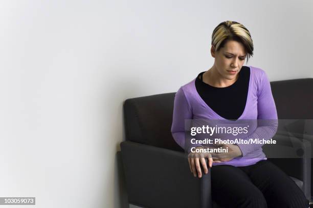 woman sitting in hospital waiting room holding stomach - appendicitis stock pictures, royalty-free photos & images