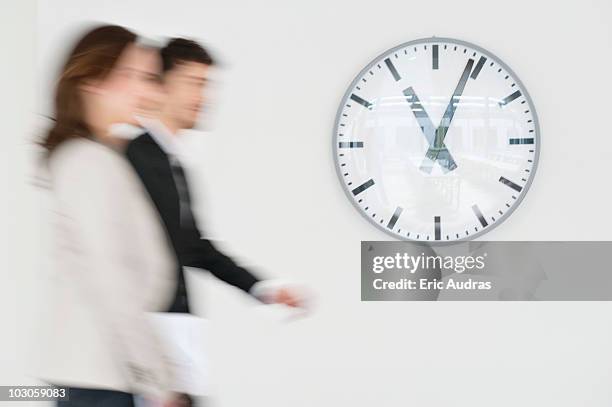business executives walking together in front of a wall clock - walking past office wall stock pictures, royalty-free photos & images