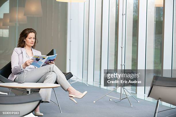 woman listening to an mp3 player and reading a magazine - holding magazine stock-fotos und bilder