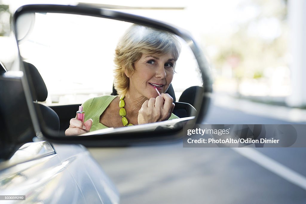 Woman putting on makeup, reflection in side-view mirror