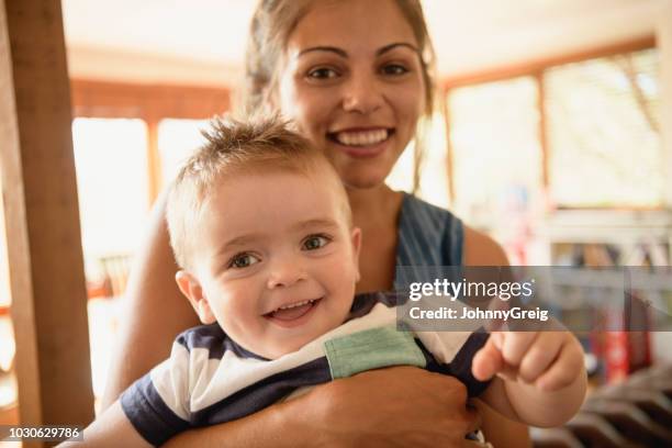 cheerful woman holding young son and smiling towards camera - australian aboriginal stock pictures, royalty-free photos & images