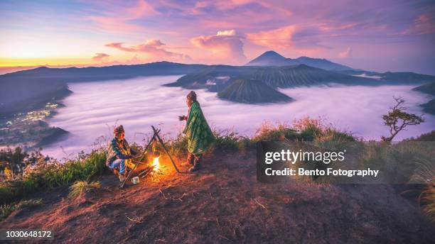 2 local indonesian doing campfire while sunrise with mt.bromo in background - mount bromo stock pictures, royalty-free photos & images