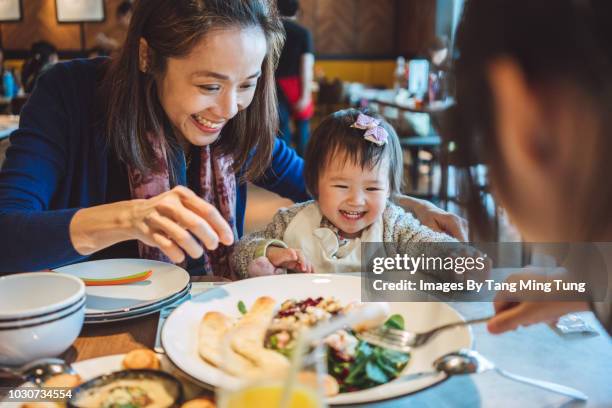 pretty young mom having veggie salad with her lovely little daughters in a restaurant joyfully. - chinese mothers day - fotografias e filmes do acervo