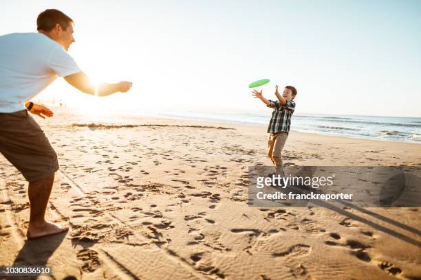 vader en zoon fresbee spelen op het strand - father son water park stockfoto's en -beelden