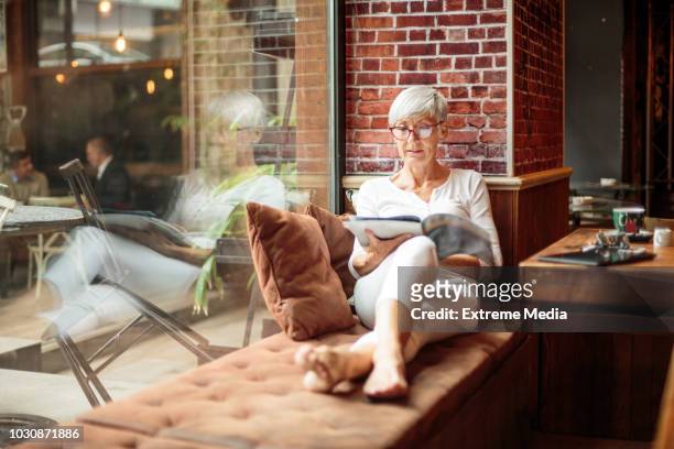 senior mujer leyendo revista en cafetería - mujer revista fotografías e imágenes de stock