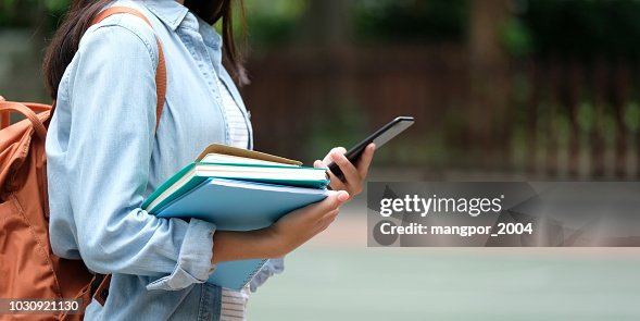 Student girl holding books and smartphone while walking in school campus background, education, back to school concept Student girl holding books and smartphone while walking in school campus background, education, back to school concept