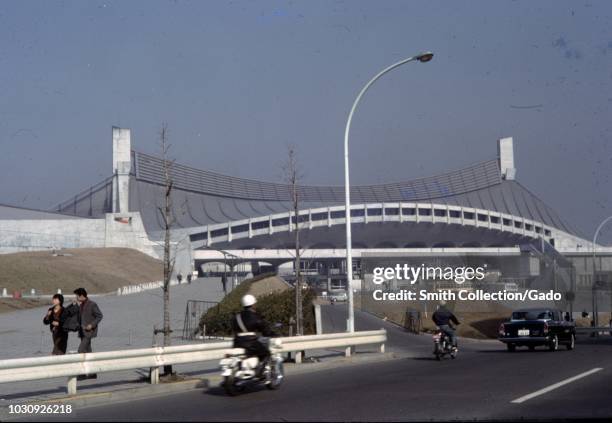 People drive and walk past the then newly constructed Yoyogi National Stadium, the site of Japan's 1964 Olympic Games, Tokyo, Japan, 1963.