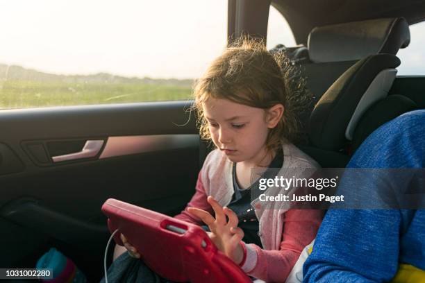 young girl using tablet device in car - girl in car with ipad stock pictures, royalty-free photos & images