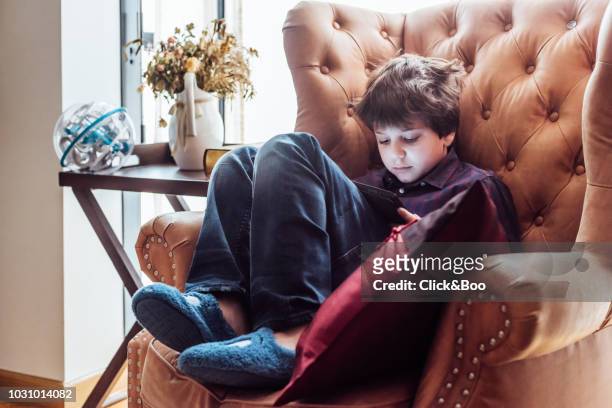 nine years old boy with tablet in an armchair indoors (home interior) - 8 9 years stock-fotos und bilder