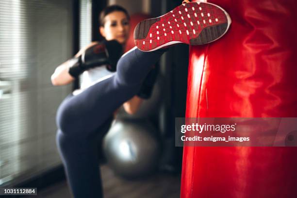 mujer pateando bolsa de boxeo en gimnasio - kick boxing fotografías e imágenes de stock