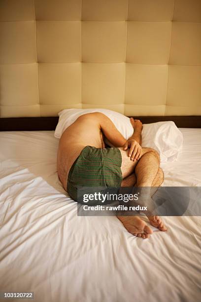 man lying in fetal position on bed - curled up stock-fotos und bilder