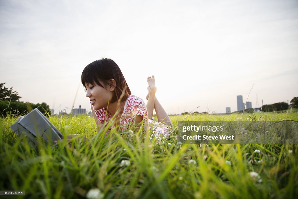 Woman laying in grass reading a book