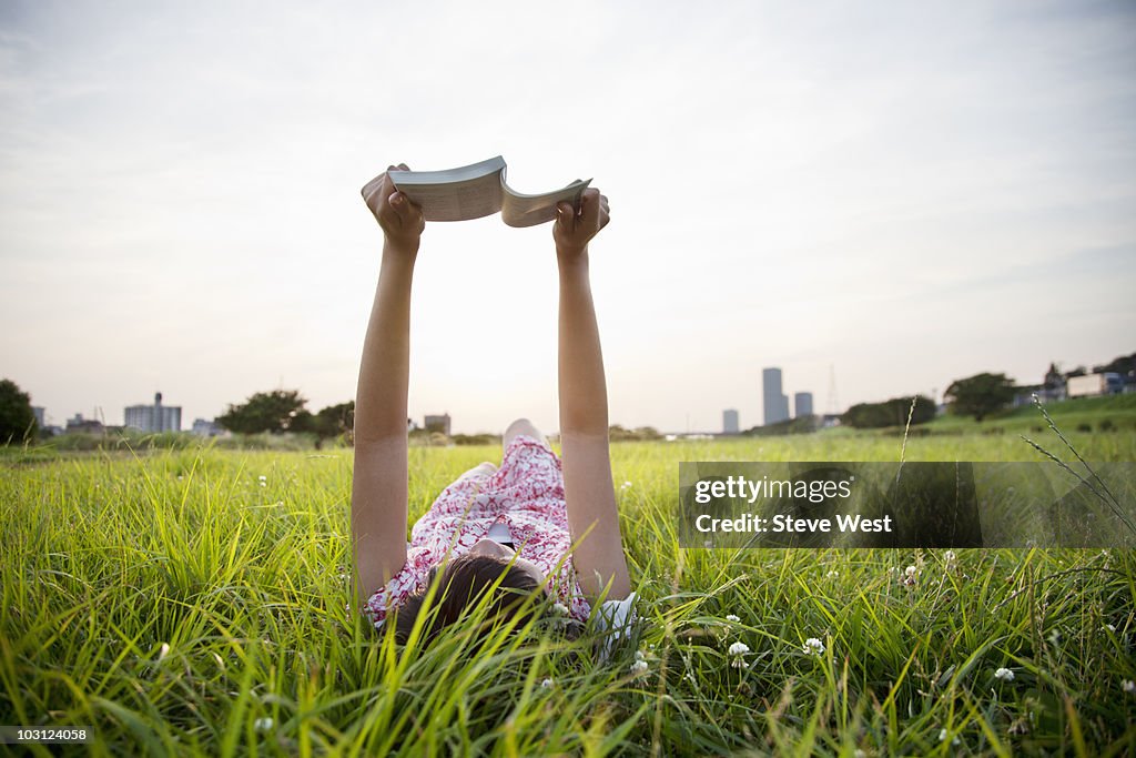 Woman laying in grass reading a book