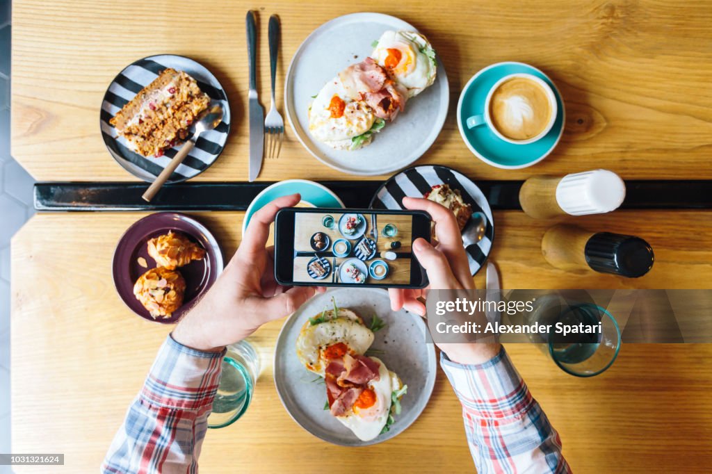 Personal perspective view of man photographing his brunch in cafe with smartphone