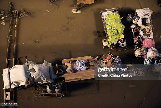 People sleep outdoors with their belongings in the parking lot of a freight yard submerged by floods, near where the Yangtze River and Hanjiang River...