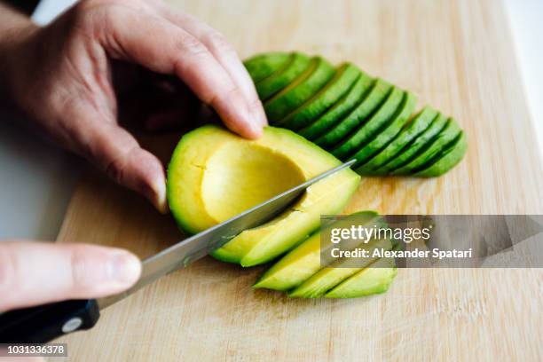 man slicing avocado with a knife on a cutting board close up - avocado fotografías e imágenes de stock