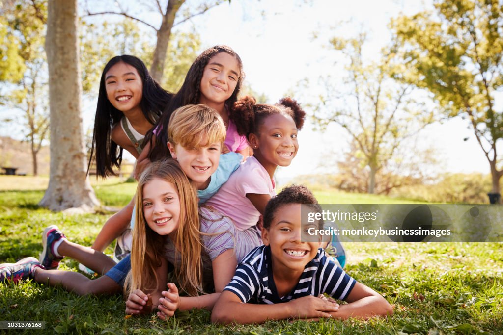 Multi-ethnic group of kids lying on each other in a park