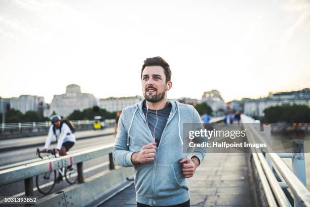 young sporty man with earphones running on the bridge outside in a city. - jogging city stock-fotos und bilder