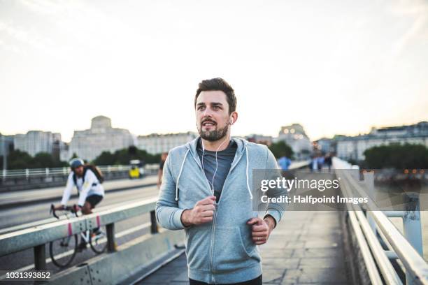 young sporty man with earphones running on the bridge outside in a city. - man running city stockfoto's en -beelden