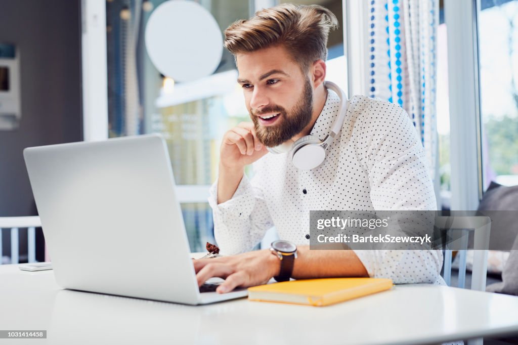 Handsome young man working on laptop while sitting in modern cafeteria