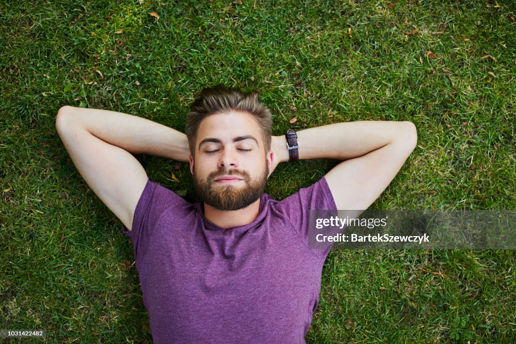 Young man lying on ground in park outdoors with eyes closed