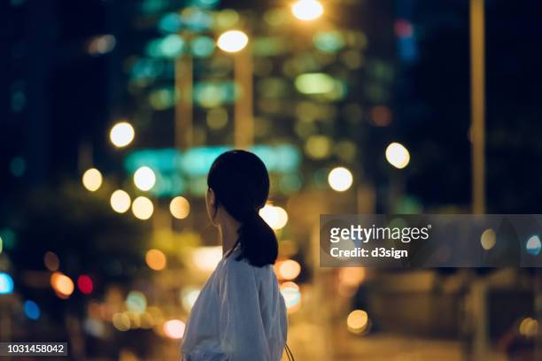 rear view of young woman looking towards illuminated city skyline at night - human prosperity stock pictures, royalty-free photos & images