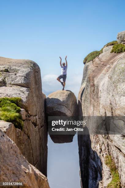 hiker standing on kjeragbolten over lyseford in norway - kjeragbolten stock pictures, royalty-free photos & images
