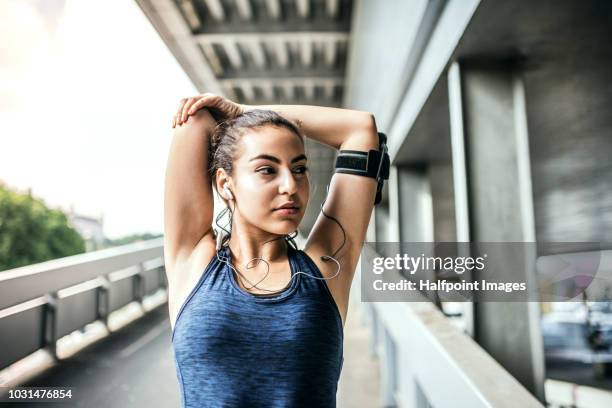 a young woman with smartphone in an arm band standing outdoors in the city, stretching. - sport armbinde stock-fotos und bilder