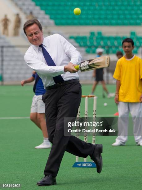 British Prime Minister David Cameron bats against the bowling of Kapil Dev during a tour of the Dhyan Chand National Hockey Stadium on July 29, 2010...
