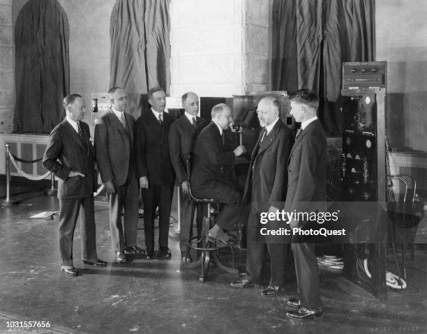 Surrounded by unidentified others, American telecommunications executive President of AT&T Walter Sherman Gifford participates in a video telephone...