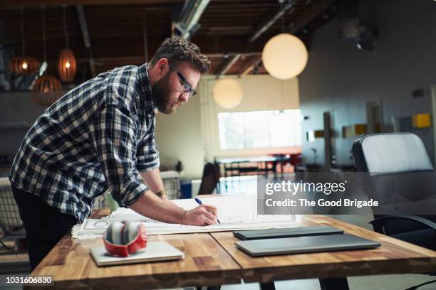 architect drafting blueprint at table in office - architect photos et images de collection