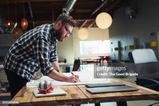 architect drafting blueprint at table in office - architetti foto e immagini stock