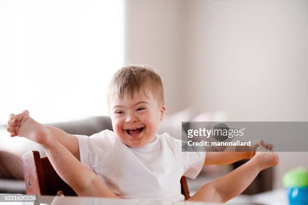 il dolce ragazzo della sindrome di down si siede al tavolo in sala da pranzo - legs on the table foto e immagini stock