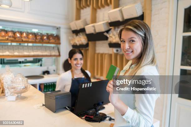 schöne weibliche kunden in einer bäckerei mit einer kreditkarte blick auf kamera und verkäuferin, die darauf warten, die bestellung zu bearbeiten - customer loyalty stock-fotos und bilder